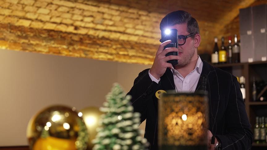 Ein Mann fotografiert etwas in einem festlich dekorierten Raum mit dem Handy, dessen Blitz gerade aktiv ist.