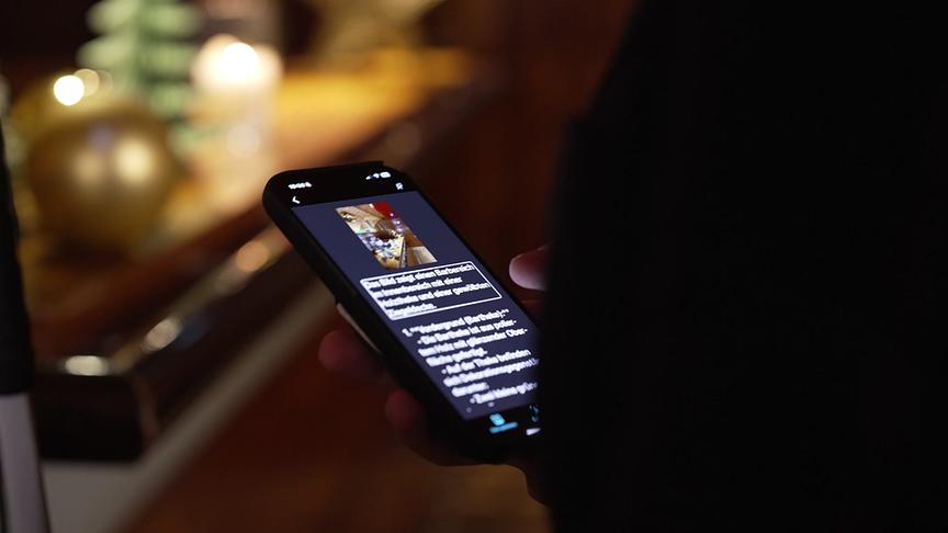 Ein Mann hält ein Smartphone in der Hand und liest die Bildbeschreibung auf dem Bildschirm.