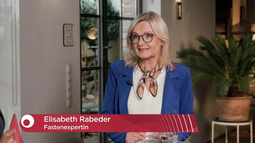 Die Fastenexpertin Elisabeth Rabeder steht in einem Innenraum und spricht vor der Kamera, begleitet von einer Grafik, die ihren Namen zeigt.