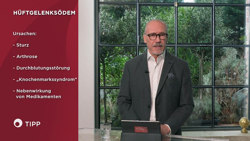 Prof. Dr. Siegfried Meryn steht im Studio neben einer medizinischen Informationsgrafik zu den Ursachen eines Hüftgelenksödems.