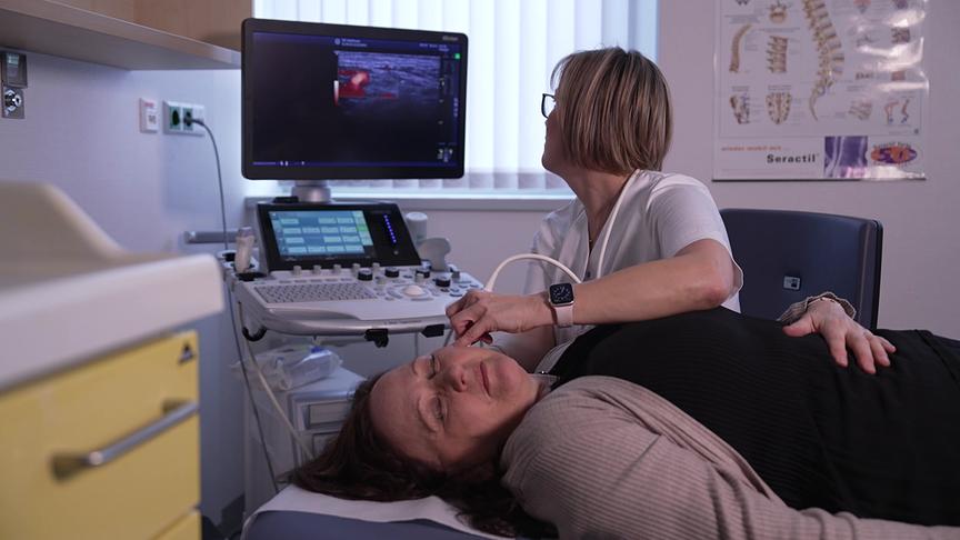 In einem Behandlungszimmer führt eine Ärztin eine Ultraschalluntersuchung bei einer liegenden Patientin durch.