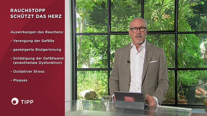 Prof. Dr. Siegfried Meryn steht an einem Tisch im Studio und gibt Informationen, wie Rauchstopp das Herz schützt, die grafisch links eingeblendet sind.