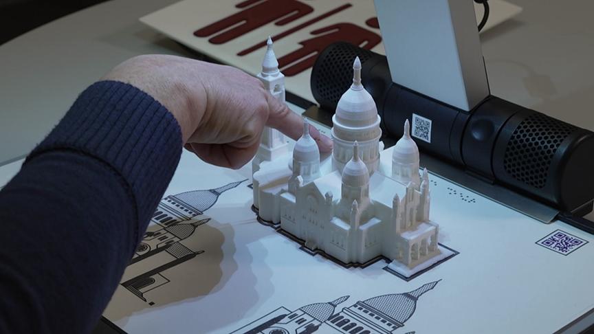 Eine Hand ertastet ein detailreiches, weißes 3D‑Modell eines historischen Gebäudes auf einer interaktiven Oberfläche.