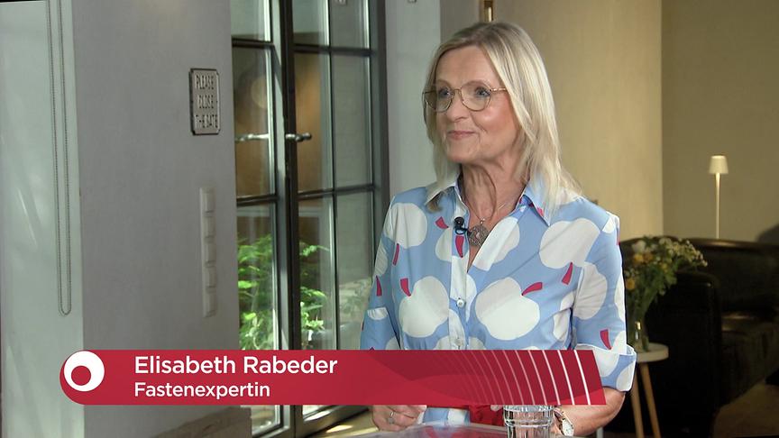 Elisabeth Rabeder beim Interview im Studio, eingeblendet ist eine rote Bauchbinde mit ihrem Namen und der Berufsbezeichnung Fastenexpertin.
