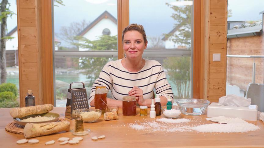 Christine Reiler sitzt an einem Holztisch mit Kren, Honig und weiteren Zutaten für ein Hausmittel.