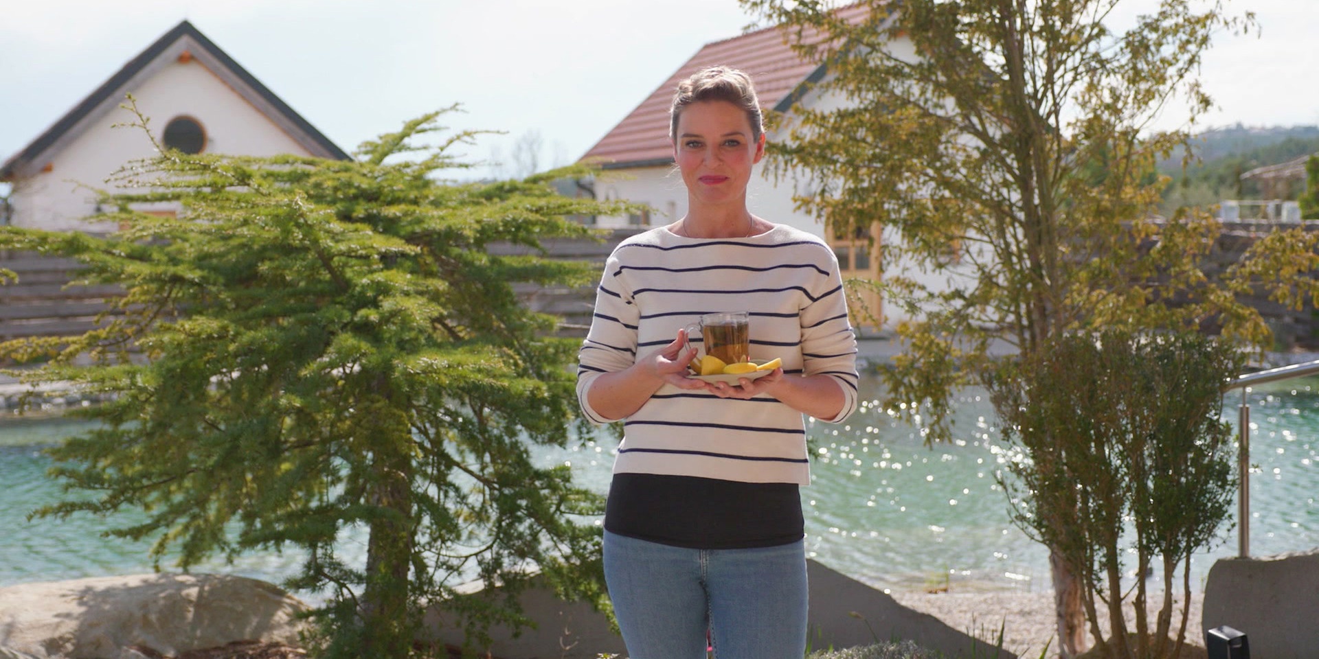 Christine Reiler steht an einem See und hält eine Tasse Tee mit Zitronenscheiben in den Händen.