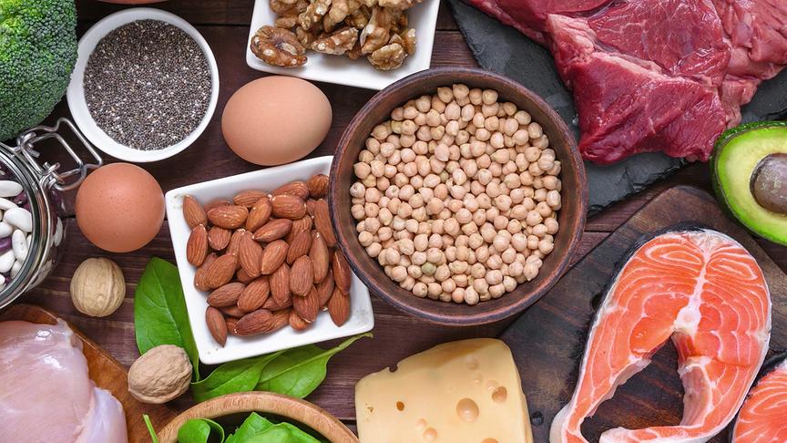 Eiweißreiche Lebensmittel wie Kichererbsen, Nüsse, Eier, Lachs, rohes Fleisch und Käse sind arrangiert.