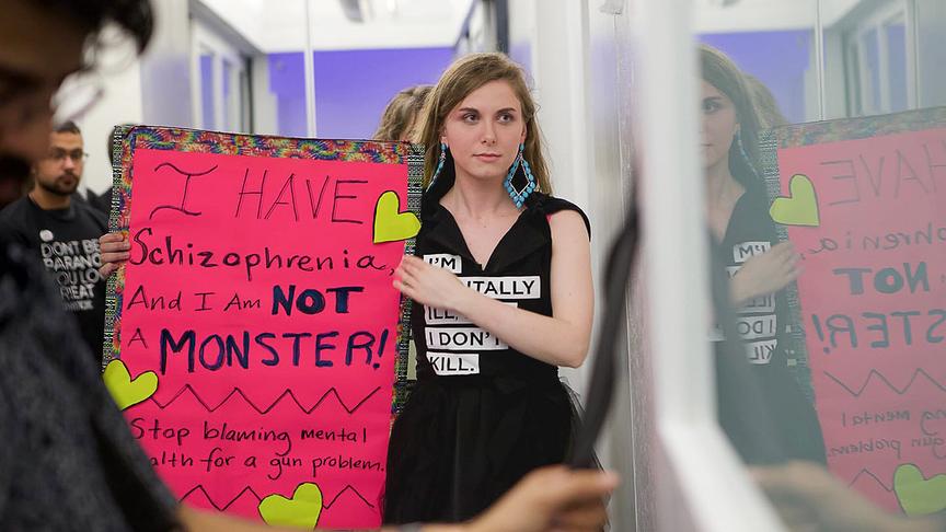Cecilia McGough hält ein Plakat hoch, das für einen differenzierten Umgang mit Schizophrenie und gegen deren Stigmatisierung wirbt.