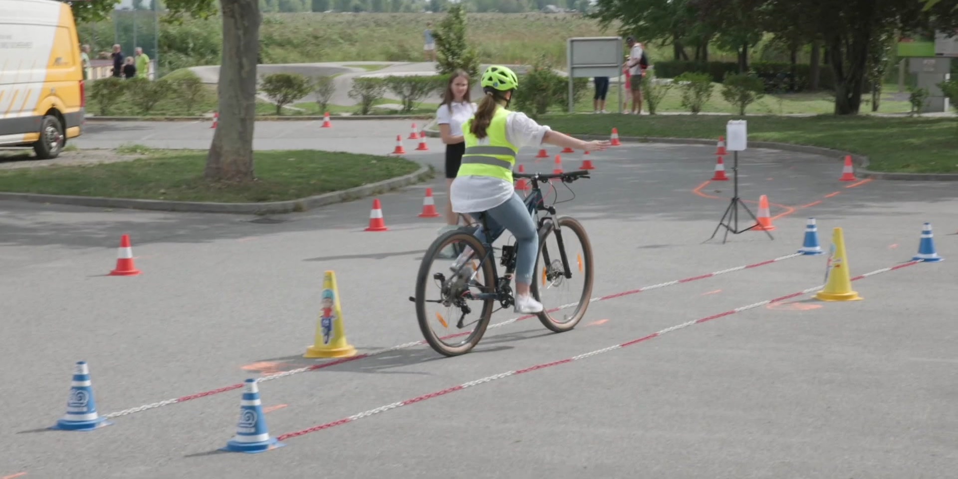 Ein Kind mit Helm und Warnweste fährt auf einem abgesperrten Parcours zwischen Pylonen Fahrrad.