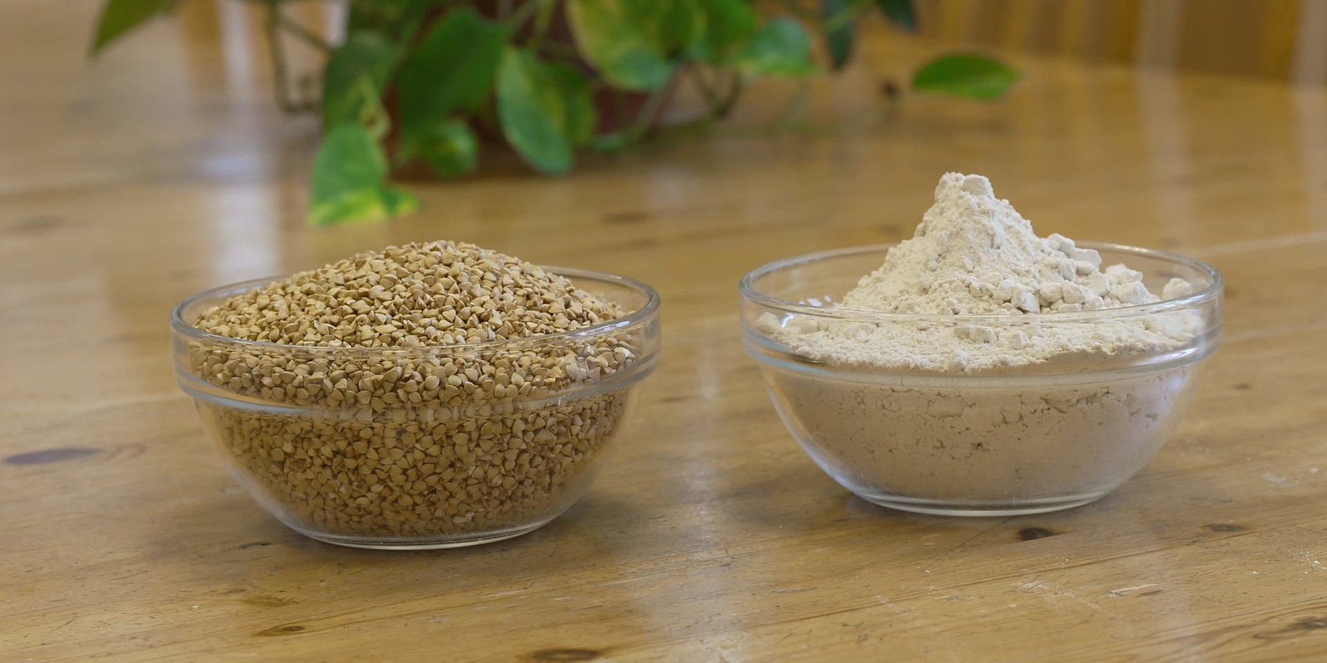 Zwei Glasschüsseln mit Buchweizen und Buchweizenmehl stehen auf einem Holztisch.