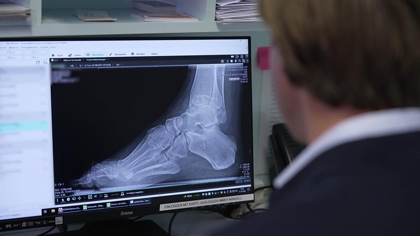 Ein Mann betrachtet ein Röntgenbild eines Fußes auf einem Computerbildschirm.