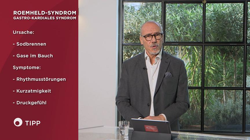 Prof. Dr. Siegfried Meryn  erklärt das Roemheld‑Syndrom und seine Symptome neben einer grafischen Infotafel.