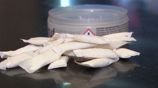 Kleine Nikotinbeutel liegen rund um eine geöffnete Dose auf einem Tisch verteilt.