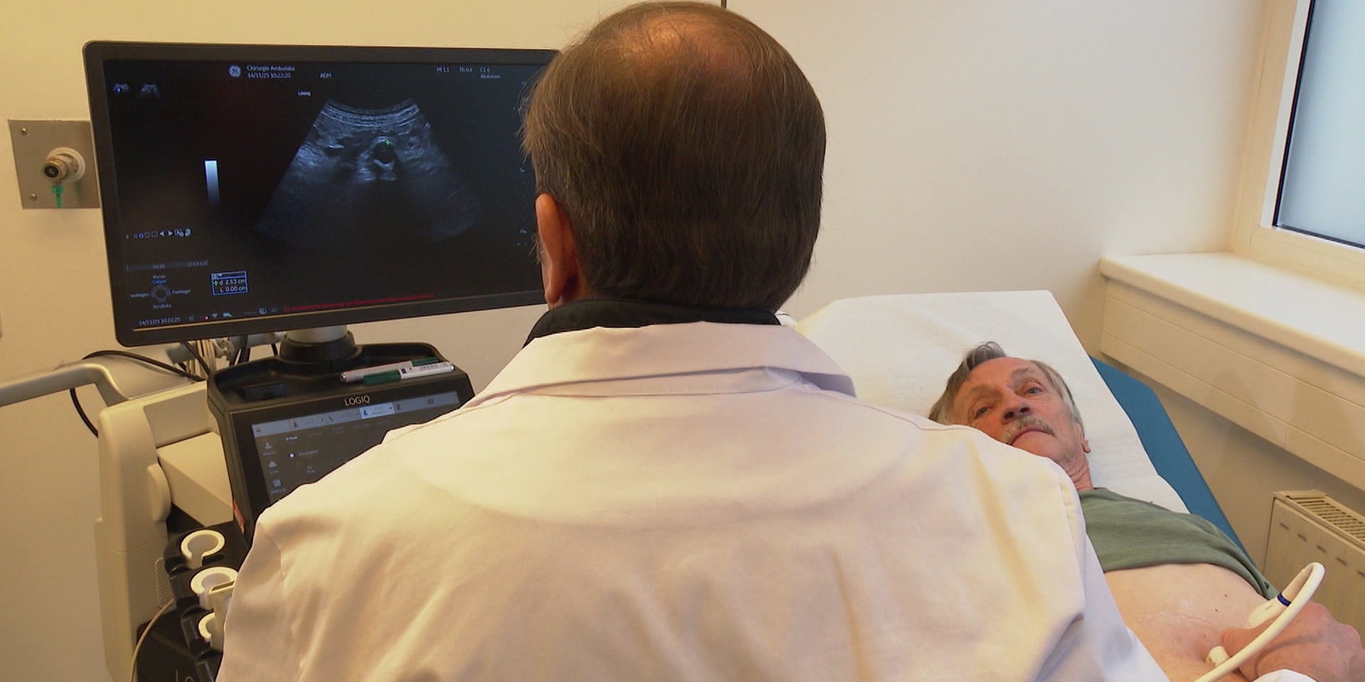 Ein Arzt führt eine Ultraschalluntersuchung bei einem Patienten durch und betrachtet das Bild auf einem Monitor.