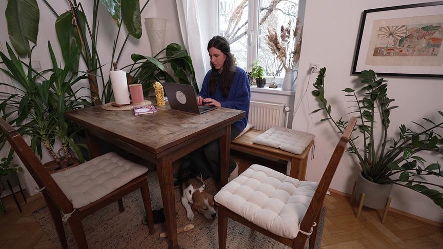 Anna-Sophie Standl arbeitet an einem Laptop in einer wohnlichen Umgebung, während ein Hund unter dem Tisch liegt.