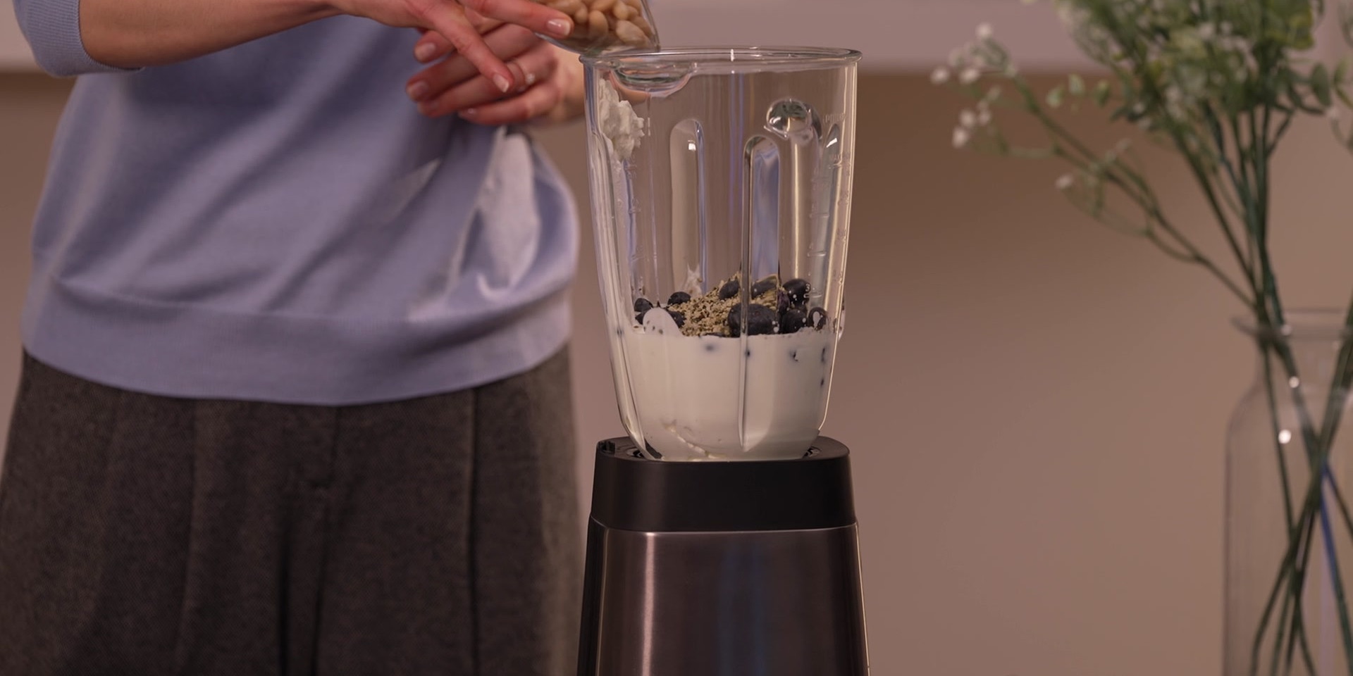 Ein Standmixer gefüllt mit Magertopfen, Kefir, Beeren, Hanfsamen und Bohnen steht auf einem Tisch.