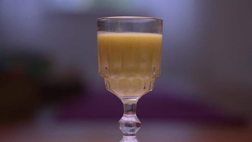 Ein Glas mit dem cremigen gelblichen Eierlikör mit Safran und Tonkabohne steht vor einem weich unscharfen Hintergrund.