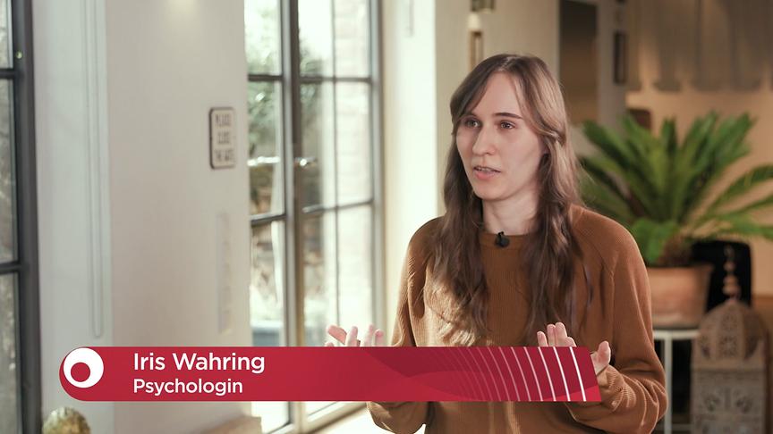 Psychologin Iris Wahring spricht in einem Wohnraum-ähnlichen Studio, ihr Name und ihre Funktion sind im Bild eingeblendet.