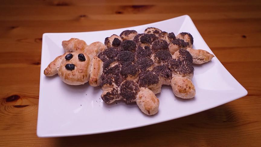 Ein Mohnweckerl in Lammform liegt auf einem rechteckigen weißen Teller.