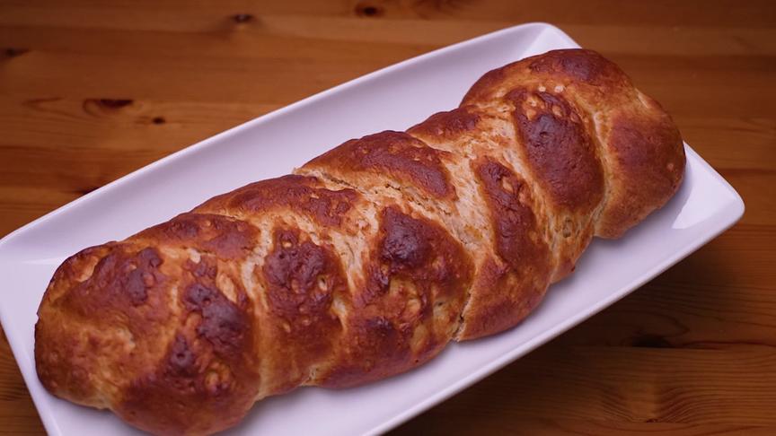 Ein goldbrauner Topfenstriezel liegt auf einer rechteckigen weißen Platte.