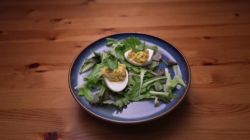 Zwei gefüllte Eierhälften liegen auf einem Bett aus frischem Blattsalat.