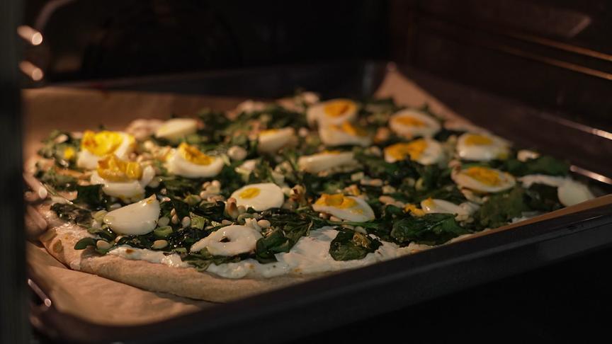 Eine Pizza mit Spinat und gekochten Eiern backt im Ofen.