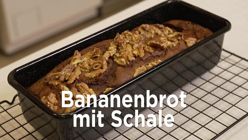 Ein frisch gebackenes Bananenbrot dekoriert mit Walnüssen liegt in einer Backform zum Auskühlen auf einem Gitter.