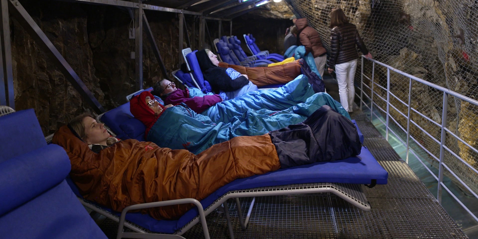 Mehrere Menschen liegen in Liegestühlen mit Decken in einem beleuchteten Heilstollen.