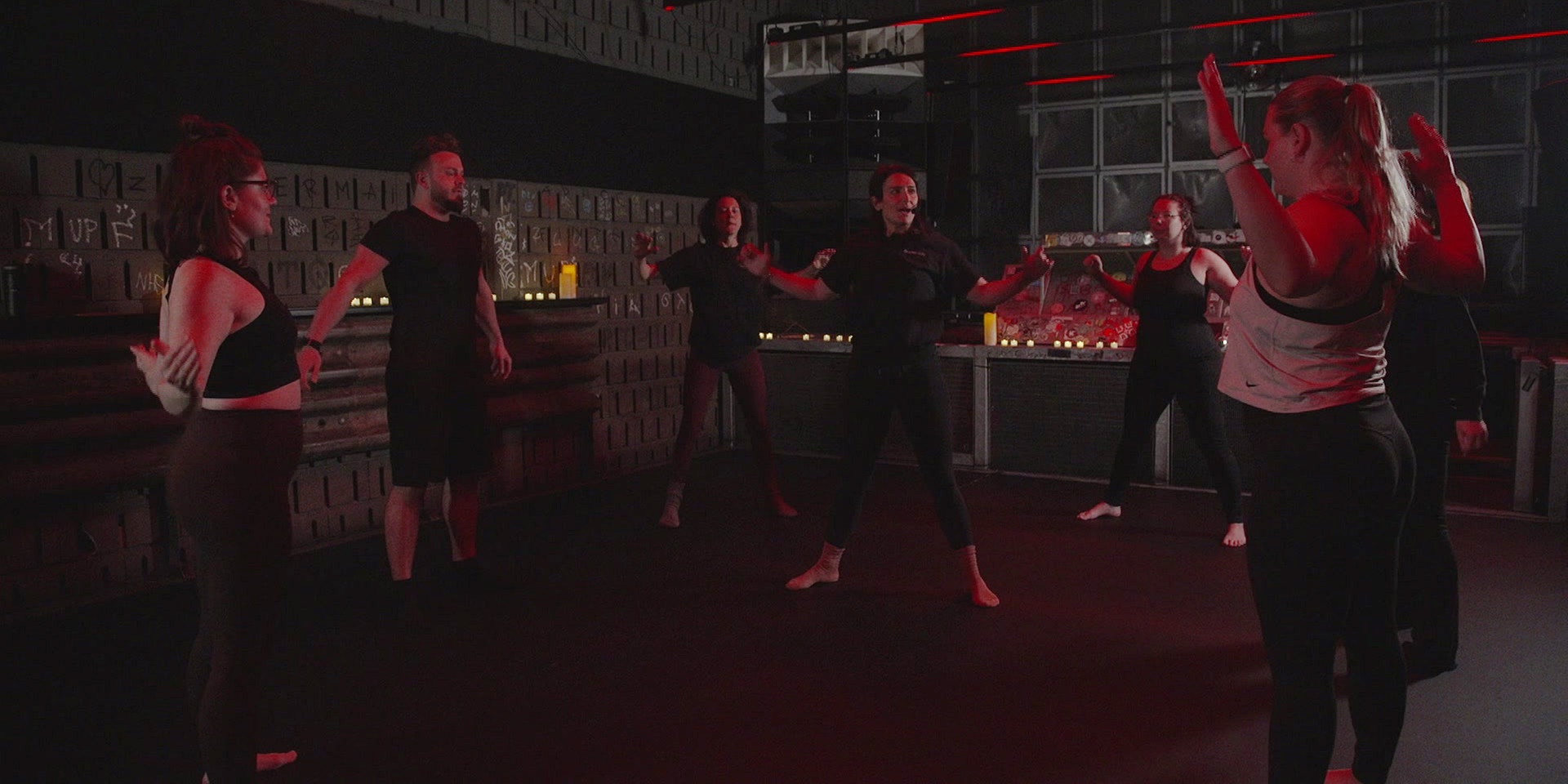 Eine Gruppe von Menschen im Fitness-Outfit und barfuß beim Tanz-Workout auf dem Dancefloor einer Disco.