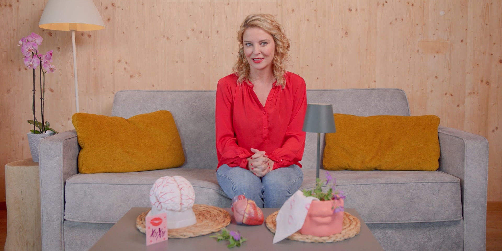 Dr. Christine Reiler  sitzt auf einem Sofa in einem wohnlich eingerichteten Raum, vor ihr stehen Modellobjekte wie ein Gehirn und ein Herz auf einem Tisch.