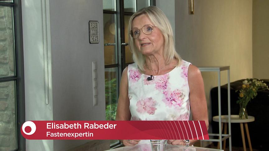 Elisabeth Rabeder beim Interview im Studio, eingeblendet ist eine rote Bauchbinde mit ihrem Namen und der Berufsbezeichnung Fastenexpertin.