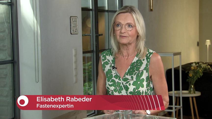 Elisabeth Rabeder beim Interview im Studio, eingeblendet ist eine rote Bauchbinde mit ihrem Namen und der Berufsbezeichnung Fastenexpertin.