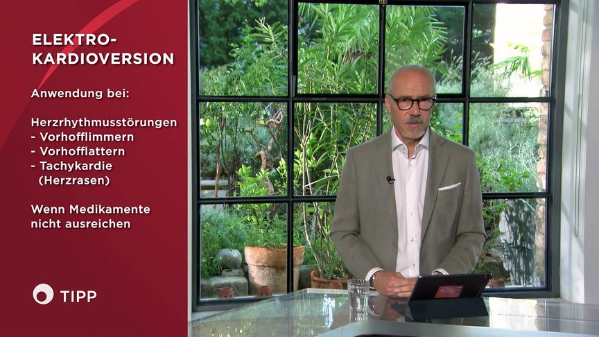 Prof. Dr. Siegfried Meryn informiert im Studio über die Elektrokardioversion bei bestimmten Herzrhythmusstörungen, die links in einer Infografik eingeblendet sind.