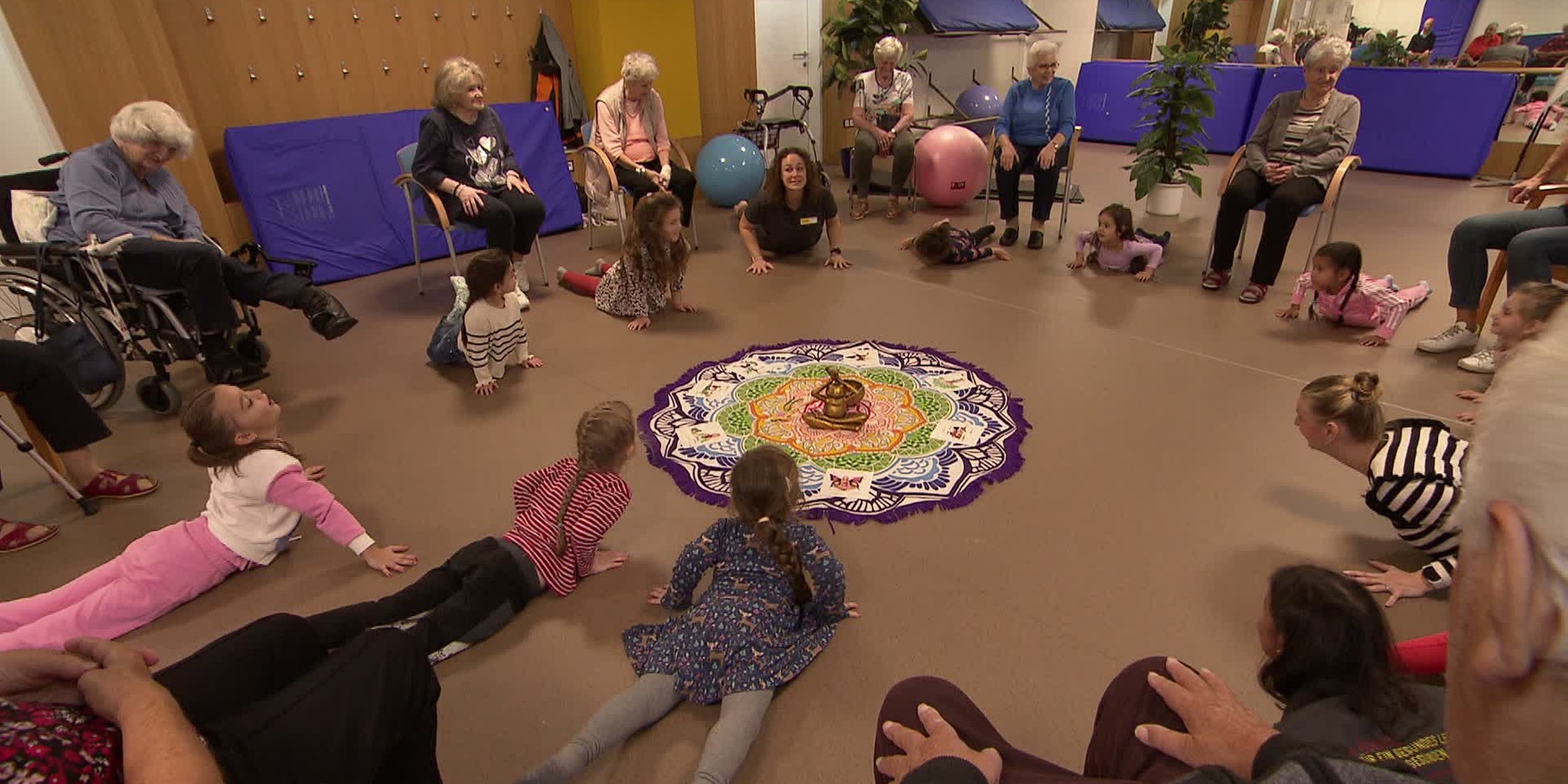 Yoga für alt mit jung: Kinder und ältere Menschen bewegen sich gemeinsam mit bunten Tüchern in einem Gruppenraum.