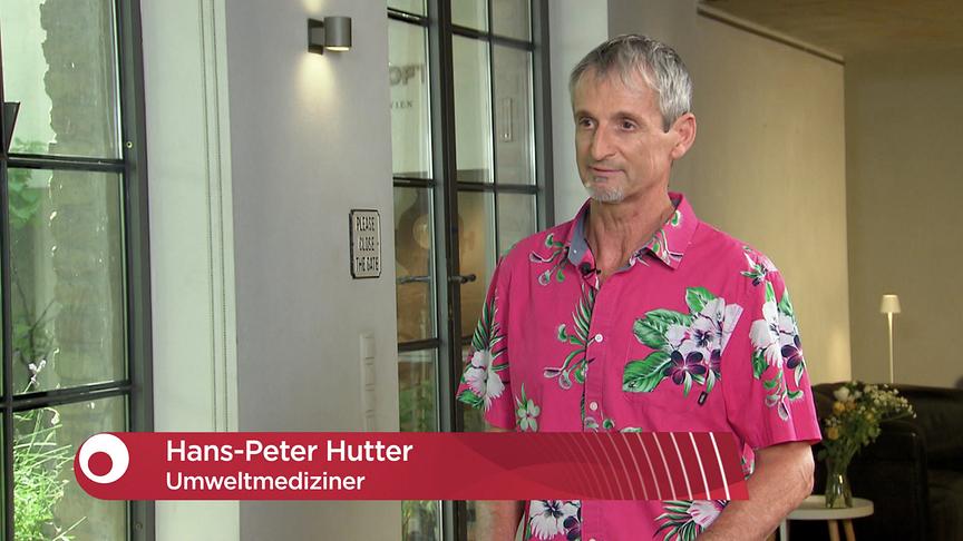 Hans Petter Hutter in einem pinkfarbenen Hawaii-Hemd steht in einem hellen Innenraum vor großen Fenstern, eingeblendet ist eine rote Bauchbinde mit seinem Namen und der Berufsbezeichnung Umweltmediziner.