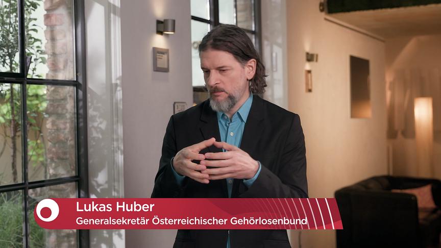 Lukas Huber, Generalsekretär des Österreichischen Gehörlosenbundes, kommuniziert in Gebärdensprache vor einer modernen Innenraumkulisse im "Bewusst gesund"-Studio.