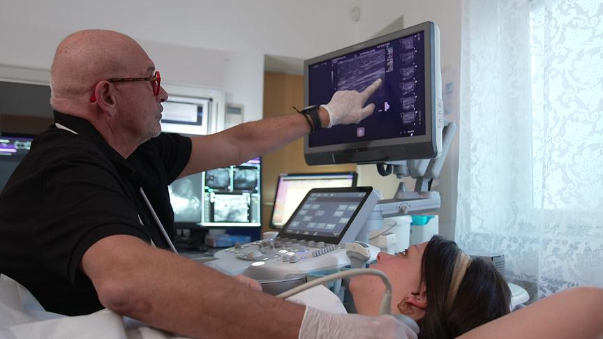 Ein Arzt führt bei einer Patientin eine Ultraschalluntersuchung durch und erklärt die Aufnahmen auf dem Monitor.