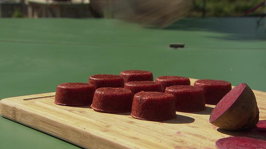 Kleine rote Rüben-Muffin liegen neben einer aufgeschnittenen Roten Rübe auf einem Holzbrett.