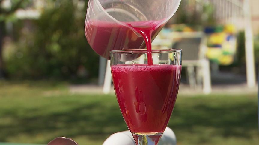 Ein leuchtend roter Rote-Rüben-Saft wird in ein Glas eingeschenkt.