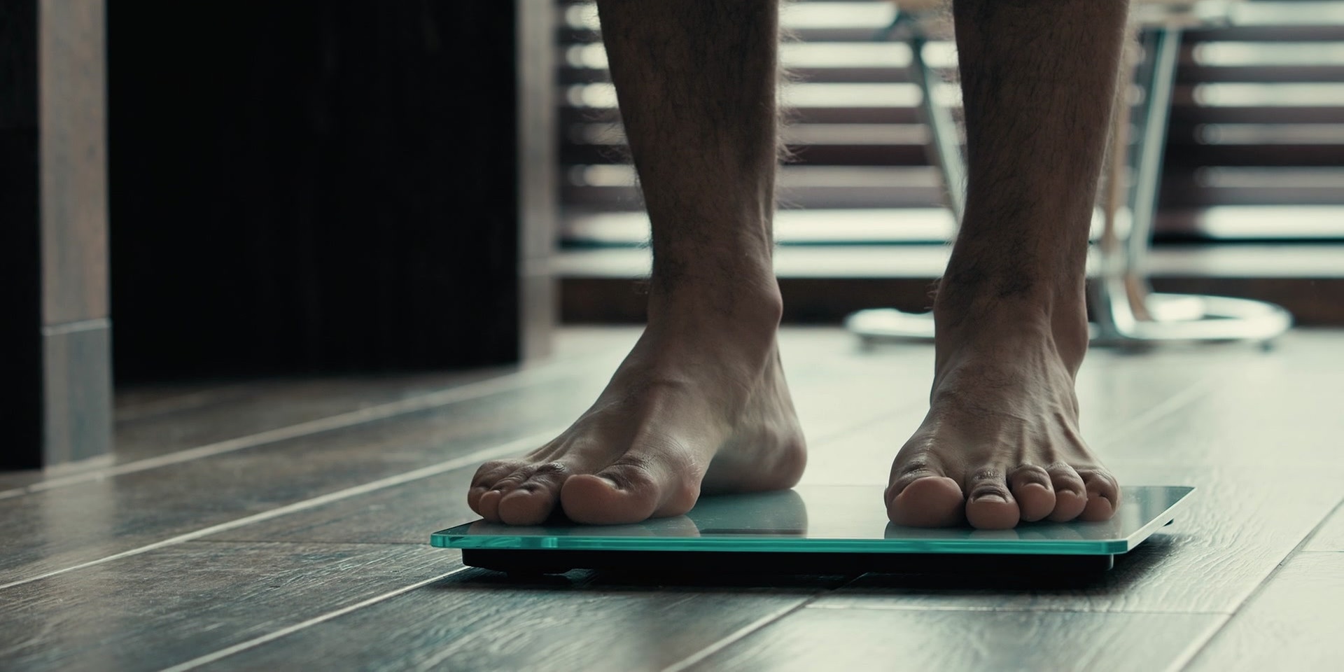 Die Füße eines Mannes auf einer digitalen Waage in einem modern eingerichteten Raum.